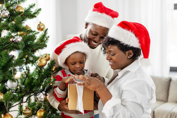 family, winter holidays and people concept - happy african american mother, father and baby son opening gift box at home on christmas