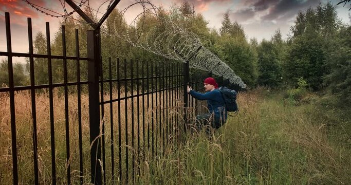 Man runs to the fence with barbed wire and climbs on it. Evening sunset. The concept of illegal border crossing, penetration into a protected object and unlawful migration
