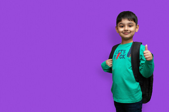 Happy smiling boy with thumb up is going to school. Child with school bag and books. Kid indoors on a background. Back to school.