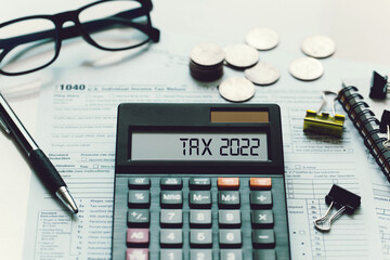 Word Tax 2022 on the calculator. Business and tax concept.Calculator, currency, book, tax form, and pen on wooden table.Top view. - obrazy, fototapety, plakaty