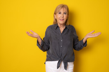 Senior age pretty woman feeling clueless and confused isolated over yellow background.