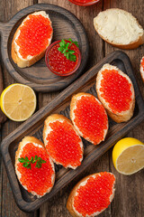 Sandwiches with red caviar in close-up and lemons on a wooden background. Top view, vertical.