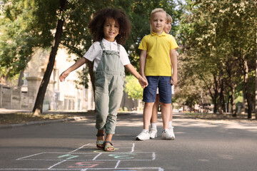 Little children playing hopscotch drawn with chalk on asphalt outdoors