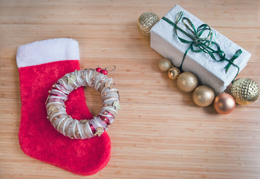 Red sock for Christmas gifts, present packed on recycled paper, golden balls decorations on table.