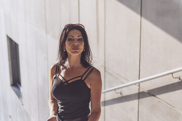 Dark-haired woman posing in a black dress on the concrete stairs. The woman is wearing black sunglasses. It's a beautiful sunny day.