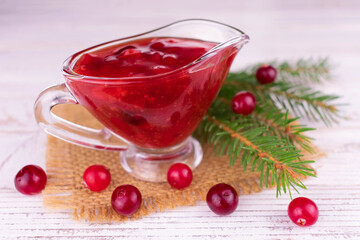 Cranberry sauce in a glass gravy boat on a white wooden background.