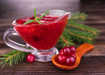 Cranberry sauce in a glass gravy boat on a wooden background.