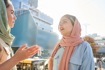 Brunette woman of islam religion telling something to her best friend wearing abaya