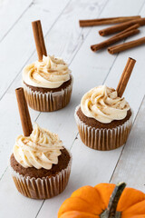 Three pumpkin spice cupcakes with cream cheese frosting and cinnamon sticks. 