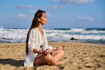 Fototapeta na wymiar Young beautiful woman in lotus position meditating on the beach