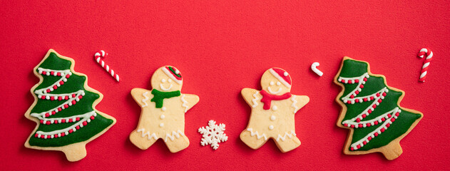 Decorated Christmas gingerbread cookies with decorations on red table background.