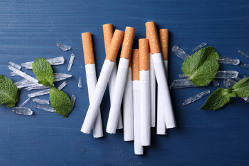 Cigarettes, menthol crystals and mint leaves on blue wooden table, flat lay