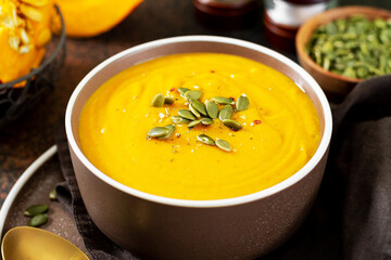 Pumpkin cream soup with seeds on a dark background. Traditional autumn vegetarian dish close-up