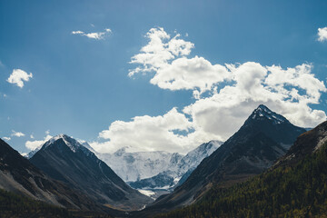 Fototapeta premium Awesome alpine landscape with snow-covered mountain tops and rocks under cloudy blue sky. Atmospheric mountain scenery with pointy peaks, snowy mountain wall and glacier in sunshine in highland valley