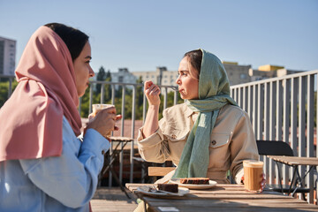 Best friends of the islamic religion eating tasty cakes at the street cafe