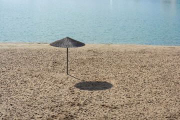 One reed umbrella on an empty beach at noon.