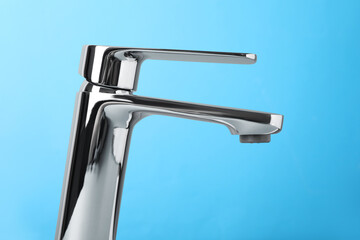 Single handle water tap on light blue background, closeup