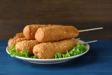 Delicious deep fried corn dogs with lettuce leaves on blue wooden table