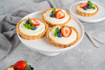 Delicious mini tarts with fresh berries and custard on a white plate on a gray concrete background. Copy space