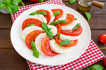 Classic caprese salad with mozzarella cheese, tomatoes and basil on a white plate on a dark wooden background. Top view, copy space.