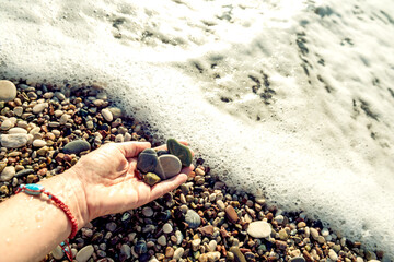 Hand with sea pebbles and sea foam and wave in sparkling sunlight.