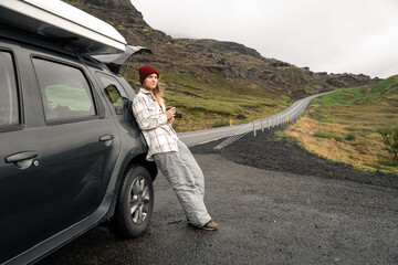 Calm young woman standing near big black car and looking into the distance
