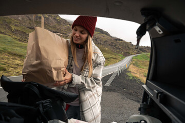 Traveller woman smiling while putting carefully heavy paper bag with food in the trunk