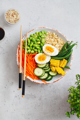 Healthy salad with couscous, carrots, cucumber, green beans, soybeans, corn and an egg on a gray concrete background. Food and health. Buddha bowl salad. Organic natural food. Plant-based dishes.
