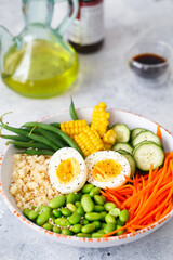 Healthy salad with couscous, carrots, cucumber, green beans, soybeans, corn and an egg on a gray concrete background. Food and health. Buddha bowl salad. Organic natural food. Plant-based dishes.