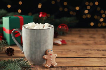 Delicious hot chocolate with marshmallows and gingerbread cookie on wooden table against blurred lights, space for text