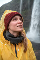 Woman stares intently into distance against backdrop of the big waterfall at the Iceland