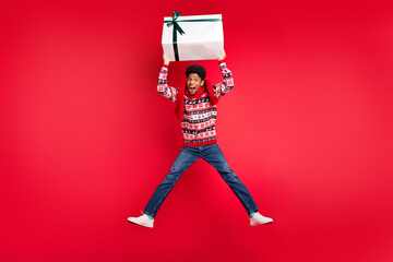 Full length photo of young afro guy happy positive smile jump hold present box spirit holiday isolated over red color background