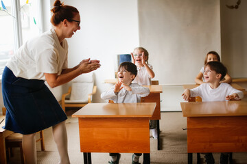 teacher with children in class beats rhythm on desks, teacher helps explain the lesson to the children in class dynamic game. Educational school process, bright room and interesting learning