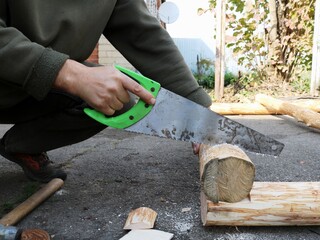sawing off a part of a log during the construction of a wooden blockhouse in a village, working with a hacksaw with wooden material, rural woodwork - obrazy, fototapety, plakaty