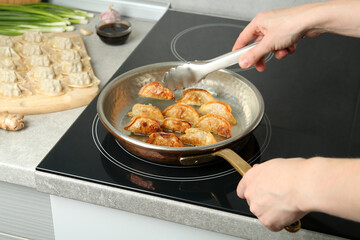 Woman cooking gyoza on frying pan with hot oil in kitchen, closeup