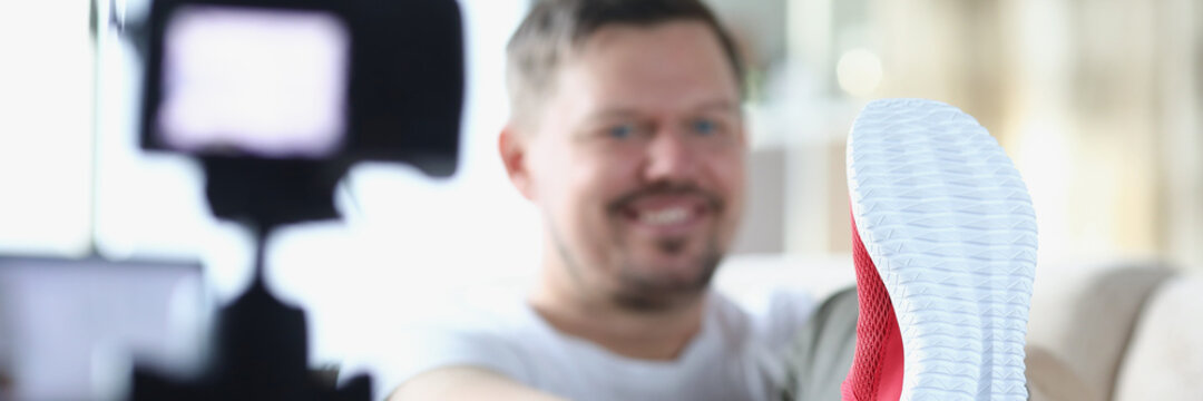 Young man putting on red sneakers in front of video camera closeup