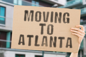 The phrase " Moving to Atlanta " drawn on a carton banner in men's hand. Human holds a cardboard with an inscription. Big city. Urban. Opportunity. Immigration