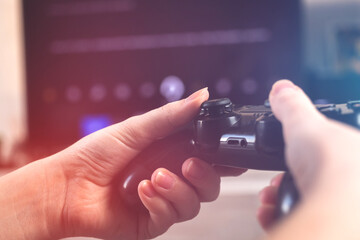 Female gamer hand playing video games on a console with wireless controller at home in cozy room sitting on sofa, close-up view of joystick
