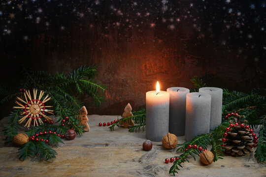 First Advent, one of four candles is lighted, Christmas decoration like nuts, straw star, cones and fir branches on rustic wood against a dark brown background, copy space