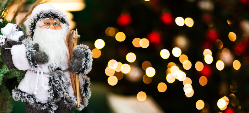 A Toy Of Santa Claus In A White Suit Stands On A Dark Background With Bokeh