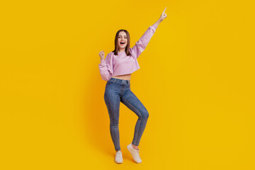 Full length photo of young attractive girl rejoice success victory indicate finger empty space isolated over yellow color background