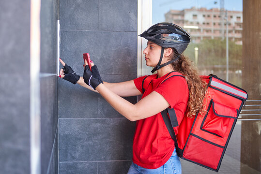 A Cyclist Delivery Girl Ringing The Intercom Bell