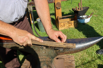 A BlackSmith Reenactment as the Craftsman Works with Metal to make a Bottle Opener for a Tourist