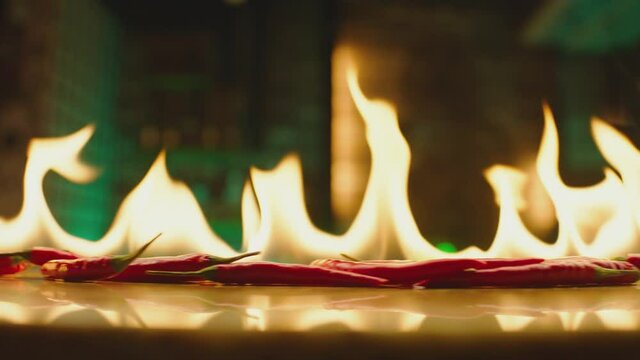 Close up shot of burning Red Chilli Peppers on table . Hot red chili peppers in flames on a restaurant background . Closeup , Slow Motion 