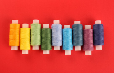 Different colorful sewing threads on red background, flat lay