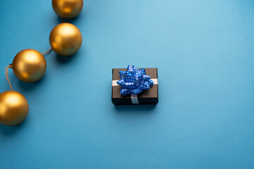 Little gift box with a blue ribbon and Christmas balls on a light blue background