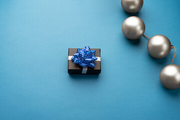Little gift box with a blue ribbon and Christmas balls on a light blue background