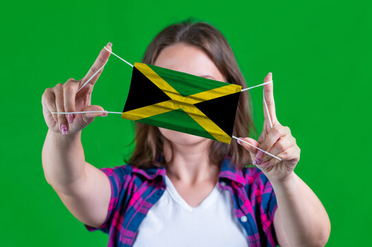Woman in a plaid shirt holds a medical mask with of the Jamaica flag on a green background