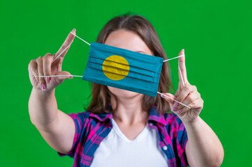 Woman in a plaid shirt holds a medical mask with of the Palau flag on a green background