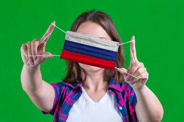 Woman in a plaid shirt holds a medical mask with of the Russia flag on a green background